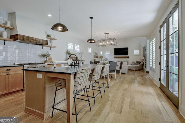 kitchen featuring premium range hood, hanging light fixtures, a kitchen breakfast bar, an island with sink, and light wood-type flooring