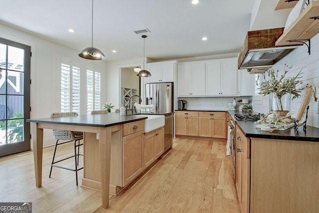 kitchen featuring appliances with stainless steel finishes, pendant lighting, an island with sink, white cabinets, and light hardwood / wood-style flooring