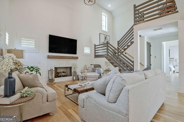 living room with a towering ceiling, a fireplace, and light hardwood / wood-style flooring