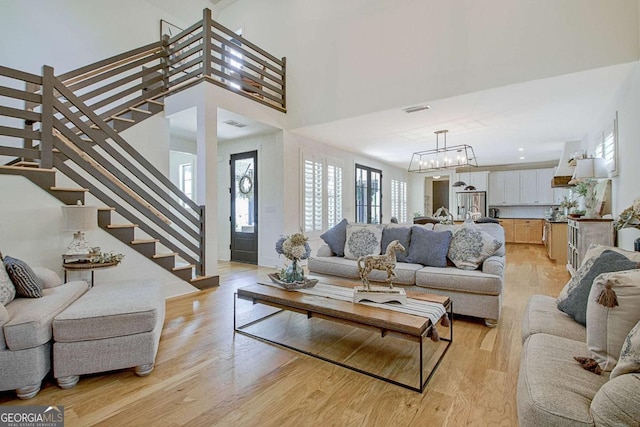 living room with an inviting chandelier, light hardwood / wood-style floors, and a high ceiling