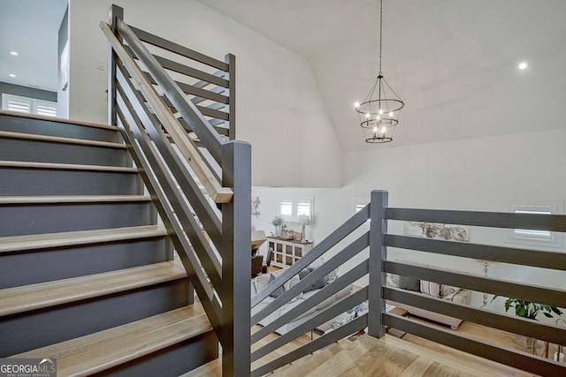 stairs with lofted ceiling, hardwood / wood-style floors, and a notable chandelier