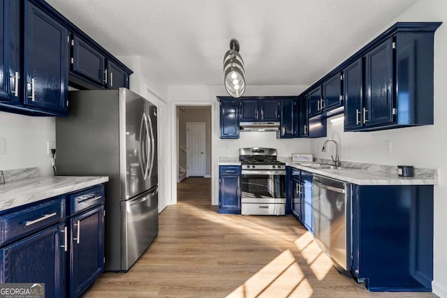 kitchen featuring appliances with stainless steel finishes, blue cabinets, sink, light wood-type flooring, and a textured ceiling