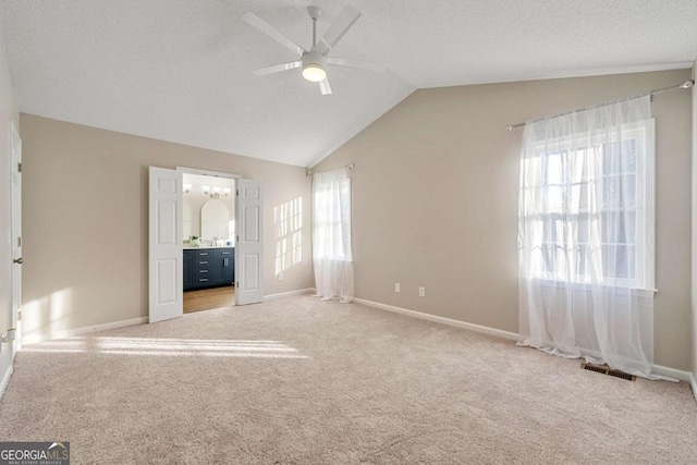 unfurnished bedroom featuring ensuite bath, ceiling fan, a textured ceiling, light carpet, and vaulted ceiling