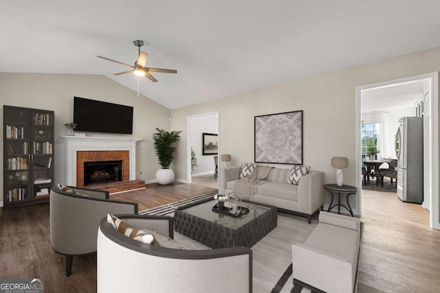 living room featuring lofted ceiling, ceiling fan, a fireplace, and wood-type flooring