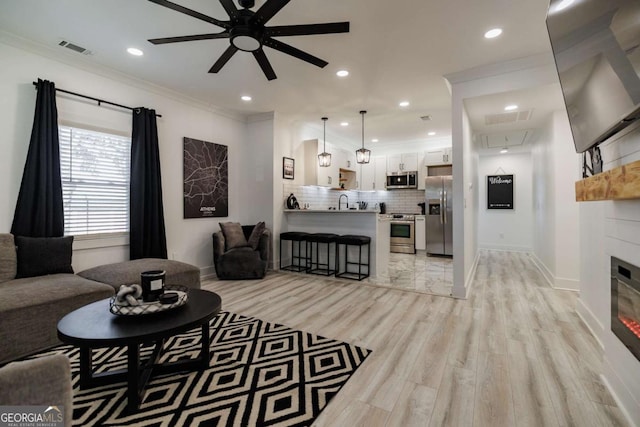 living room featuring crown molding, ceiling fan, a fireplace, and light hardwood / wood-style floors