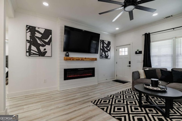 living room featuring crown molding, a large fireplace, ceiling fan, and light hardwood / wood-style floors