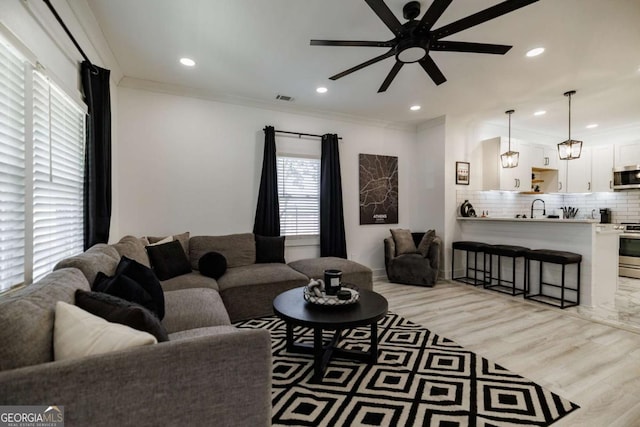 living room with sink, crown molding, light hardwood / wood-style floors, and ceiling fan