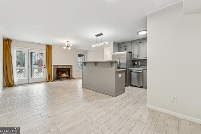 kitchen featuring light hardwood / wood-style flooring, appliances with stainless steel finishes, gray cabinets, pendant lighting, and backsplash