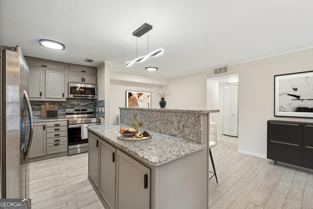 kitchen featuring appliances with stainless steel finishes, gray cabinetry, a center island, a kitchen bar, and decorative light fixtures