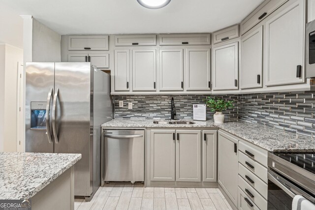 kitchen featuring tasteful backsplash, stainless steel appliances, light stone countertops, and sink