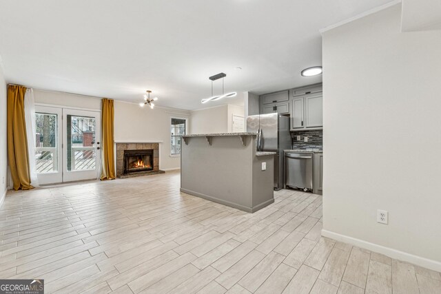 kitchen featuring decorative light fixtures, stainless steel fridge, gray cabinets, a tiled fireplace, and a kitchen island with sink