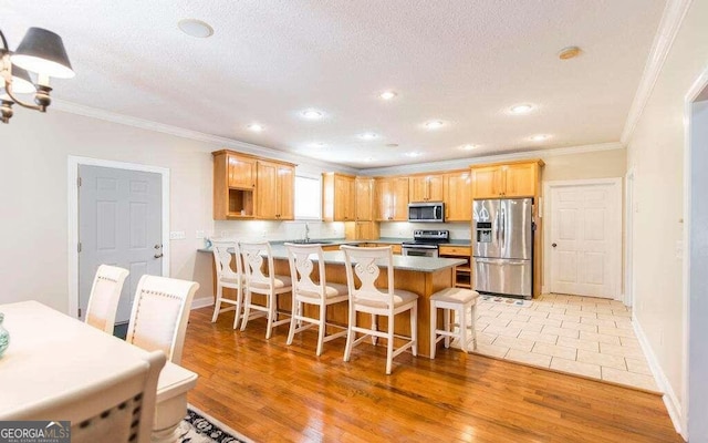 kitchen with a kitchen bar, crown molding, light hardwood / wood-style flooring, appliances with stainless steel finishes, and kitchen peninsula