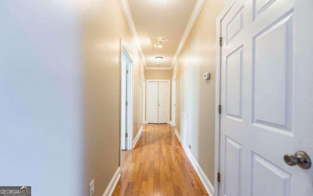 hallway with ornamental molding, a textured ceiling, and light hardwood / wood-style floors