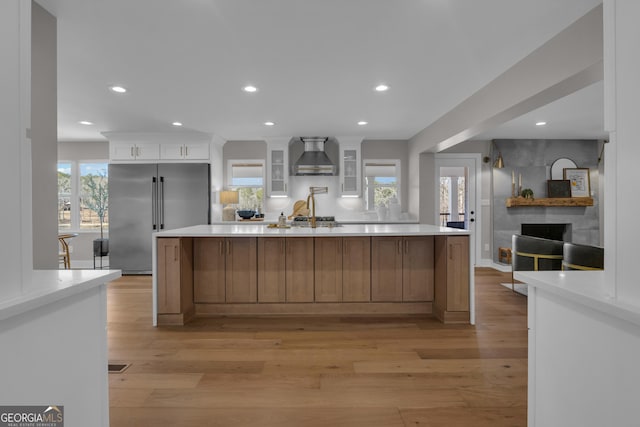 kitchen featuring appliances with stainless steel finishes, white cabinets, wall chimney range hood, light wood-type flooring, and a spacious island