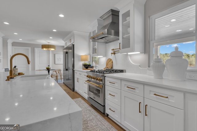 kitchen featuring sink, light stone counters, high quality appliances, wall chimney range hood, and white cabinets