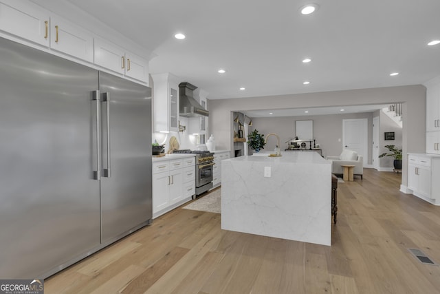 kitchen with wall chimney range hood, a spacious island, light stone counters, premium appliances, and white cabinets