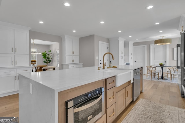 kitchen featuring stainless steel appliances, an island with sink, white cabinets, and light brown cabinets