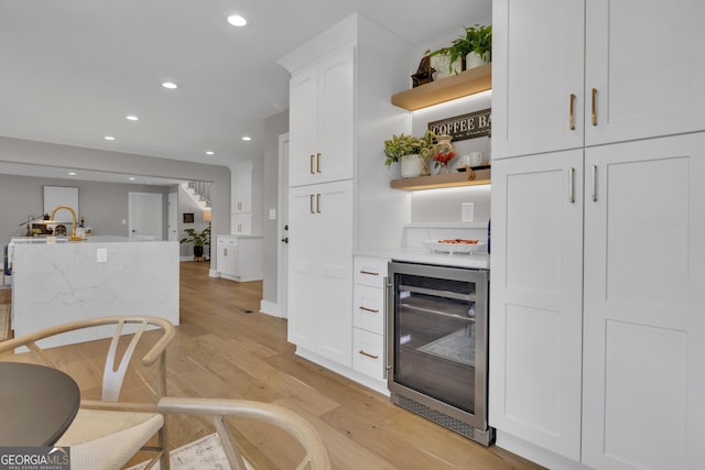 kitchen featuring wine cooler, light stone countertops, white cabinets, and light wood-type flooring