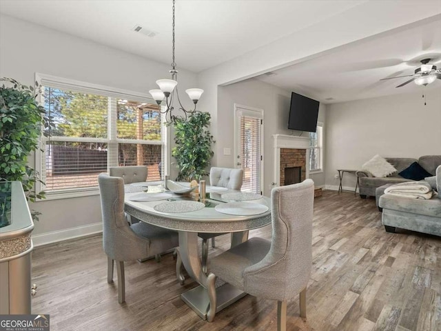 dining room featuring ceiling fan with notable chandelier, hardwood / wood-style floors, and a fireplace