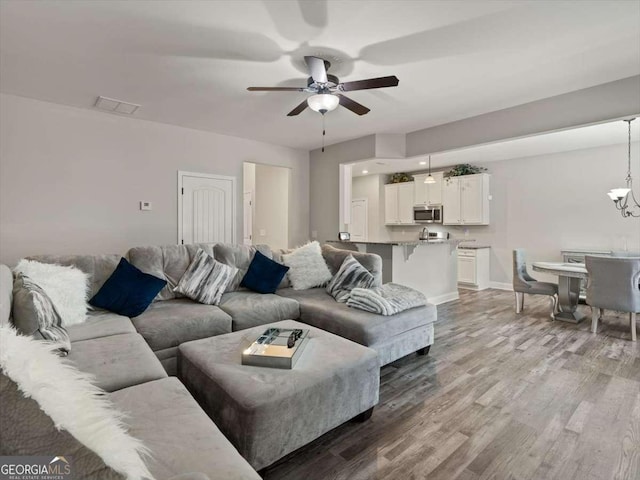 living room featuring ceiling fan with notable chandelier and light wood-type flooring