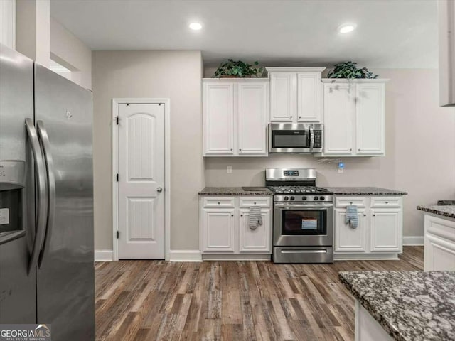 kitchen with dark hardwood / wood-style floors, dark stone counters, white cabinets, and appliances with stainless steel finishes