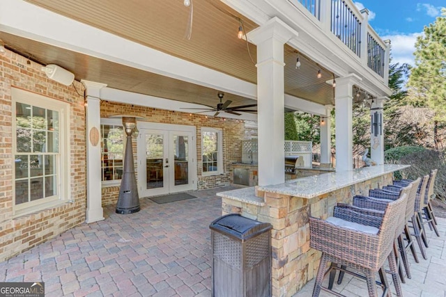 view of patio / terrace with a bar, ceiling fan, exterior kitchen, and french doors