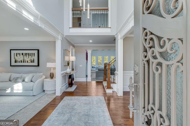 foyer entrance featuring crown molding, a towering ceiling, dark hardwood / wood-style flooring, and decorative columns