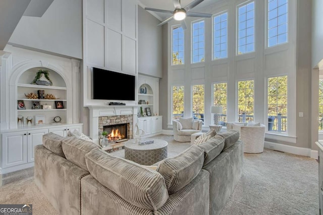 living room featuring built in shelves, a fireplace, plenty of natural light, and a high ceiling