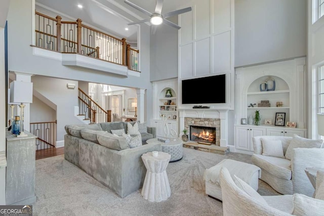 living room featuring a towering ceiling, built in features, a fireplace, decorative columns, and ceiling fan