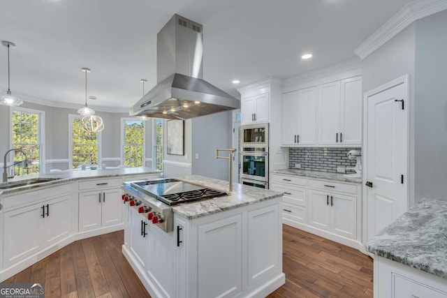 kitchen featuring appliances with stainless steel finishes, island range hood, decorative light fixtures, white cabinetry, and sink