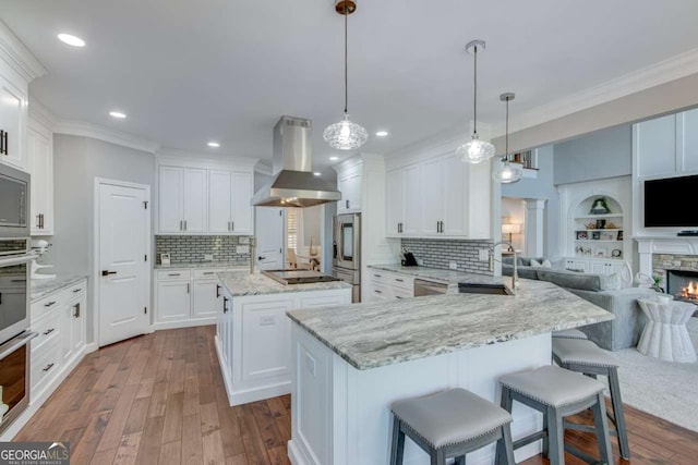 kitchen featuring sink, white cabinetry, kitchen peninsula, pendant lighting, and island exhaust hood