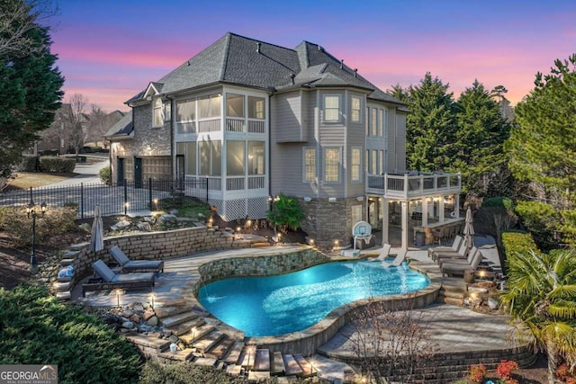 pool at dusk with a sunroom and a patio area