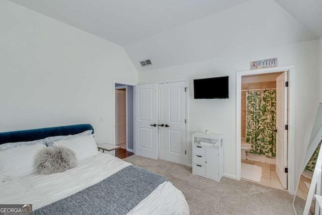 bedroom with a closet, ensuite bath, vaulted ceiling, and light carpet