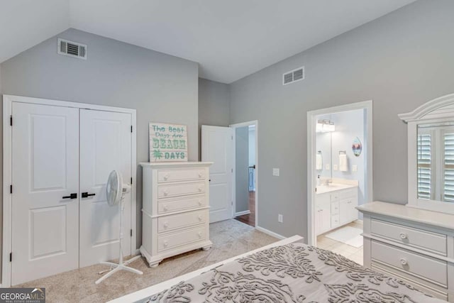 carpeted bedroom featuring ensuite bath, vaulted ceiling, and a closet