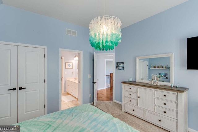 bedroom featuring an inviting chandelier, ensuite bath, light colored carpet, and a closet