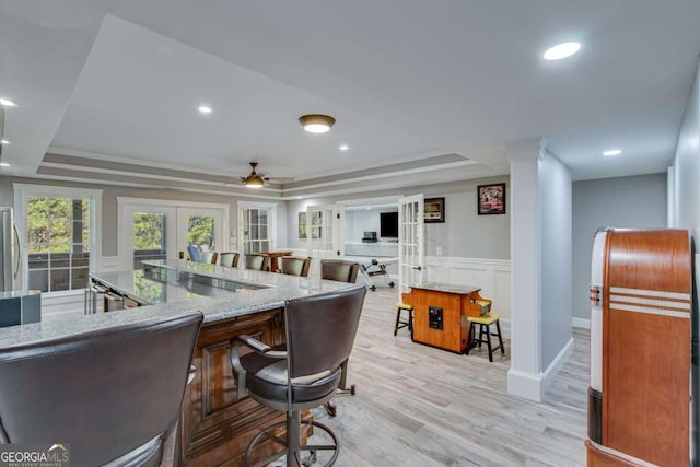 dining room featuring decorative columns, ceiling fan, a tray ceiling, light wood-type flooring, and french doors