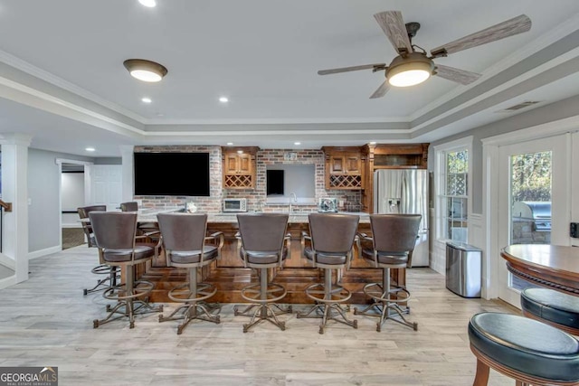 bar featuring ornamental molding, stainless steel fridge, a raised ceiling, and light hardwood / wood-style floors