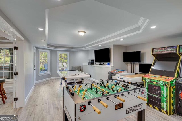 game room featuring a raised ceiling, crown molding, and light hardwood / wood-style flooring