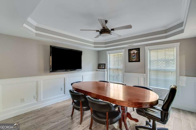 dining space featuring ceiling fan, ornamental molding, a raised ceiling, and light wood-type flooring