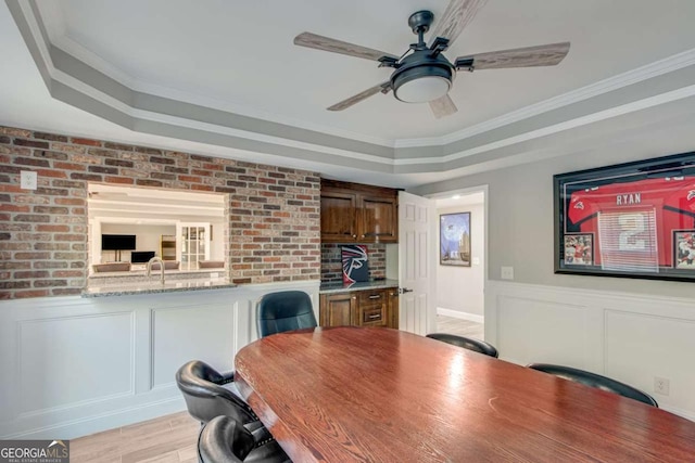 dining space with light hardwood / wood-style floors, a raised ceiling, and brick wall