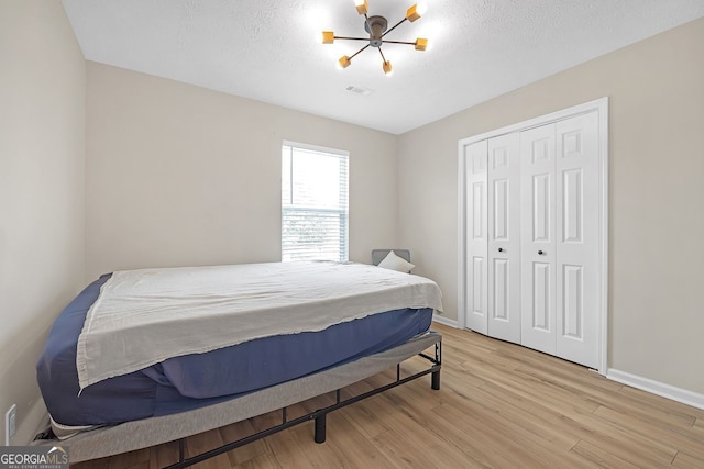 bedroom with light hardwood / wood-style floors, a closet, a textured ceiling, and a notable chandelier