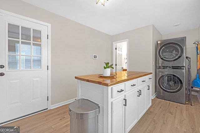 washroom featuring cabinets, stacked washer / drying machine, and light hardwood / wood-style flooring