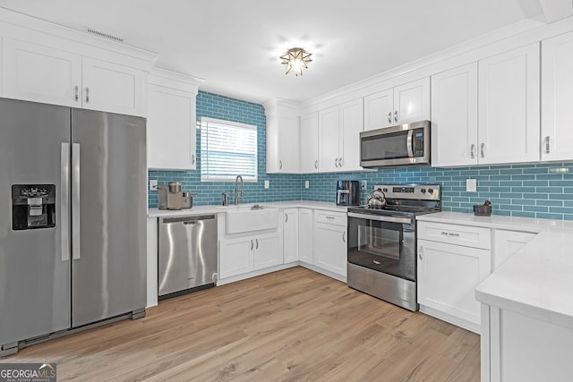 kitchen featuring light wood-type flooring, stainless steel appliances, white cabinets, decorative backsplash, and sink