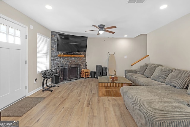 living room with ceiling fan, wood-type flooring, and a stone fireplace