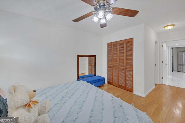 bedroom with a closet, stainless steel refrigerator, ceiling fan, and light wood-type flooring