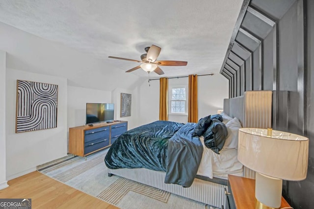 bedroom featuring ceiling fan, lofted ceiling, light hardwood / wood-style floors, and a textured ceiling