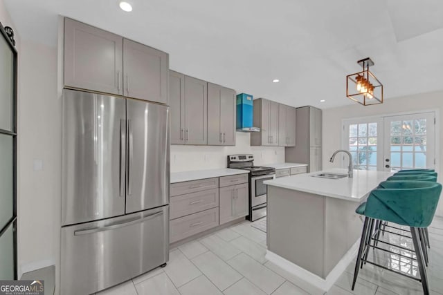 kitchen with sink, gray cabinetry, appliances with stainless steel finishes, a kitchen island with sink, and wall chimney range hood