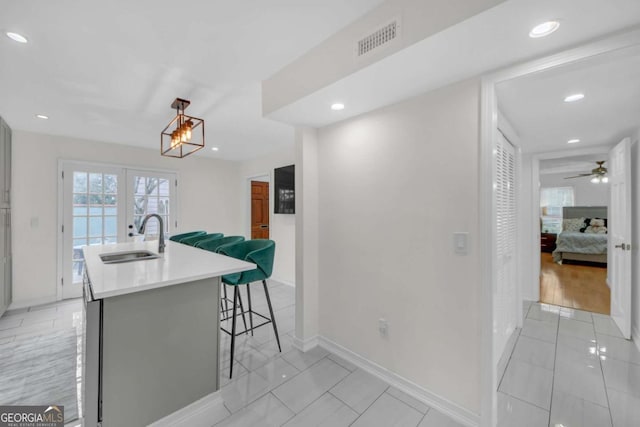 kitchen with pendant lighting, sink, a breakfast bar, ceiling fan, and a kitchen island with sink