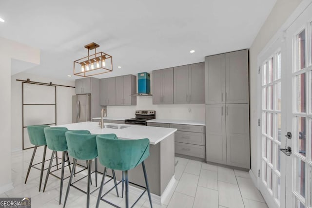 kitchen with sink, gray cabinetry, appliances with stainless steel finishes, a barn door, and wall chimney range hood