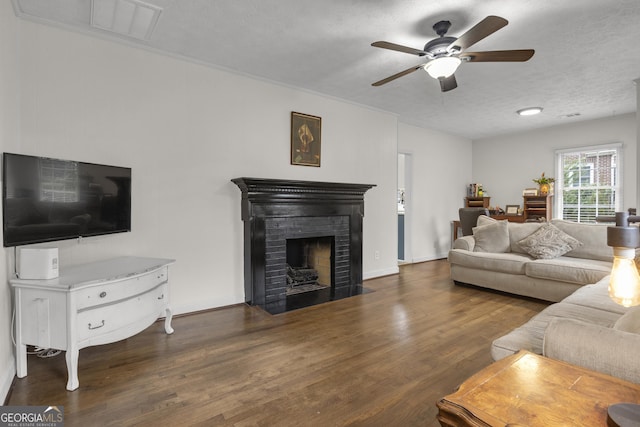 living room with ceiling fan, dark hardwood / wood-style floors, a brick fireplace, and a textured ceiling